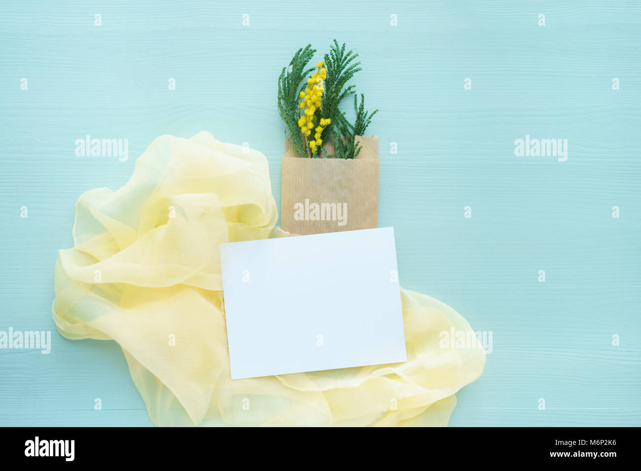 Mimosa Brunch in Kraft Umschlag Tasche in Blau auf einem Hintergrund von gelber Seide mit weißen leere Karte für Text Stockfoto