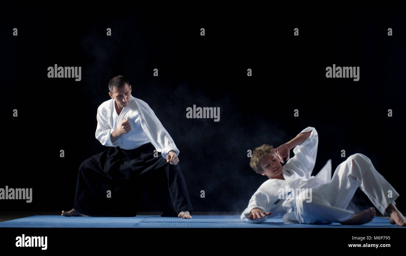 Kampfkunst Aikido Master tragen Hakamas lehrt seine Schüler, wie man sich gegen einen Angriff zu verteidigen. Schuß isoliert auf schwarzen Hintergrund. Stockfoto