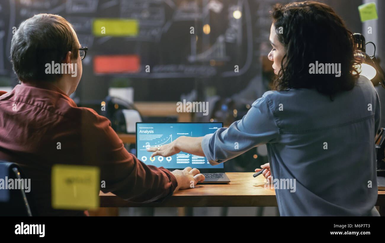 Männlichen und Weiblichen Finanziers in Statistiken und Diagrammen dargestellt auf dem Laptop schauen, Sie sprechen Probleme lösen. Im Hintergrund kreative Büro. Stockfoto