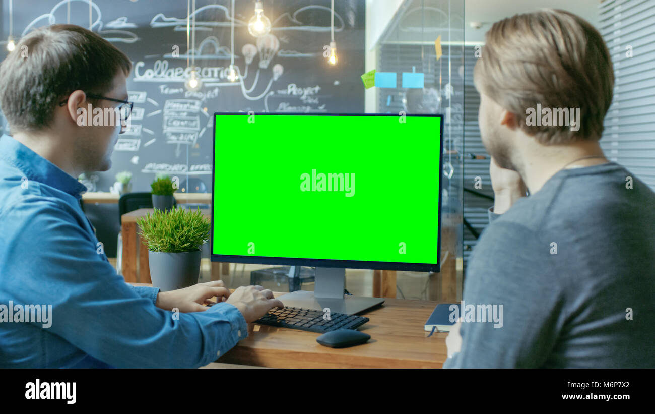 Zwei Mitarbeiter haben Projekt Diskussion, auf dem Schreibtisch steht Personal Computer mit Mock-up Green Screen. Sie arbeiten im kreativen Büro Stockfoto