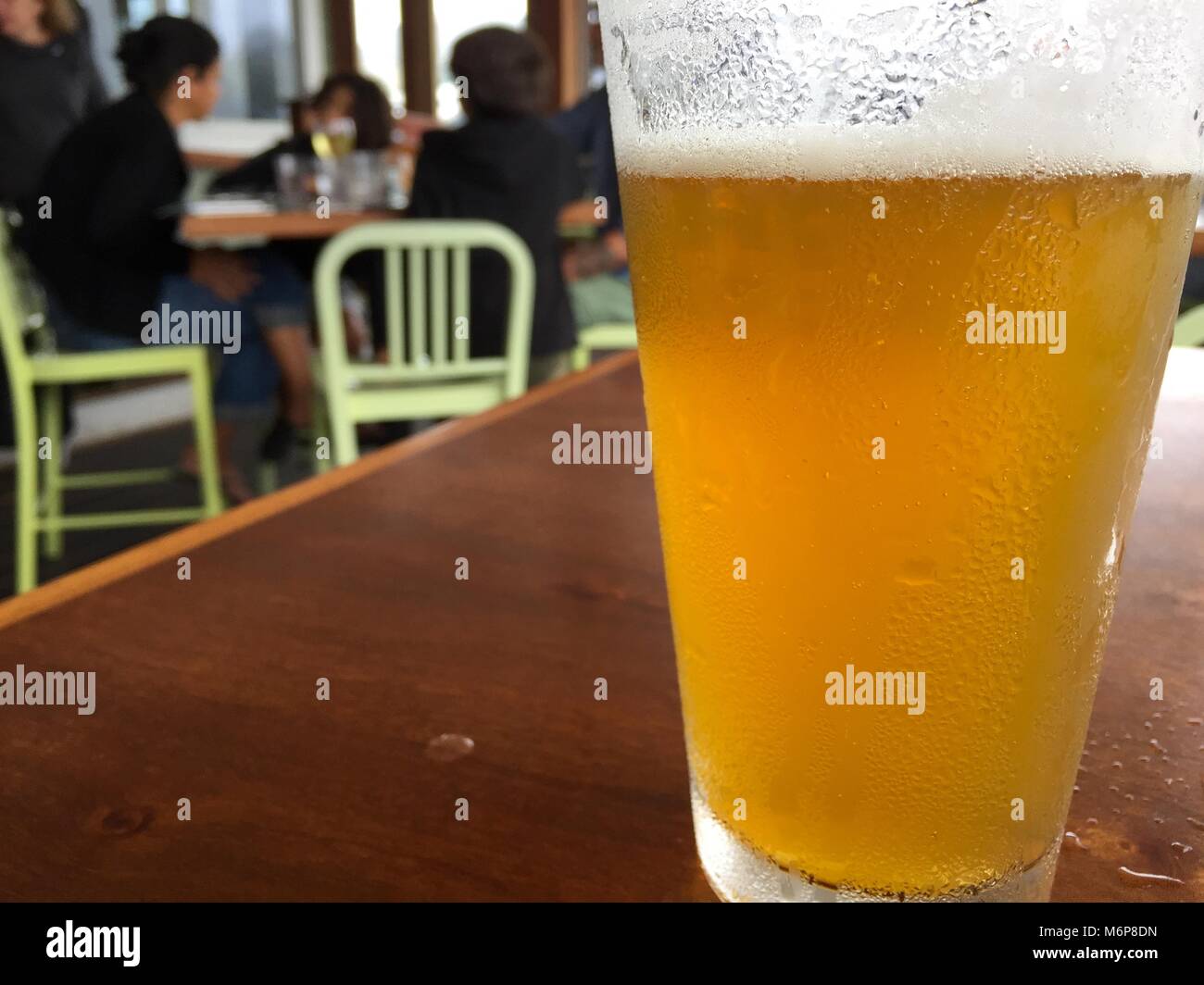 Nahaufnahme Foto von Tall Pint Bier Glas Milchglas mit leichten Lager gegossen sitzen auf Holztisch auf zwangloses Restaurant. Familie genießt Mahlzeit zusammen in Bl Stockfoto