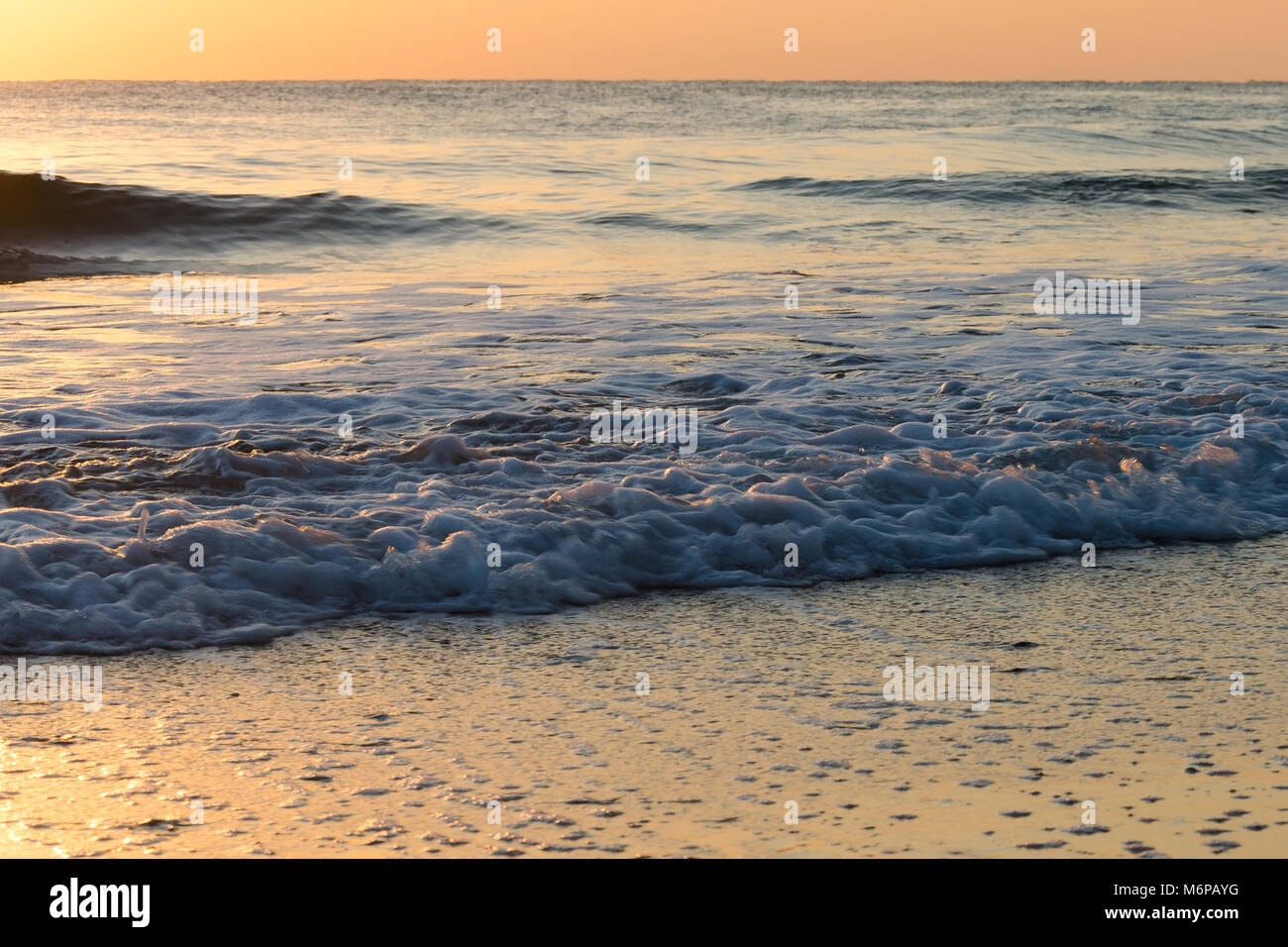 Hell erleuchtete seascape Hintergrund mit goldfarbenen sanft brechen Meer Wellen am Strand bei Sonnenaufgang Stockfoto