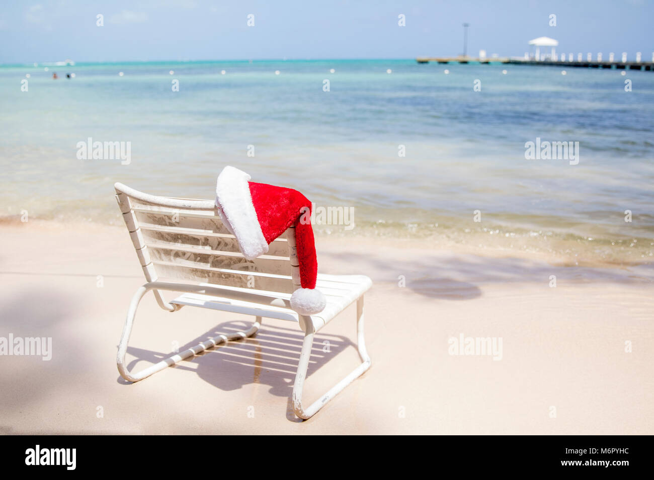 Eine Weihnachtsmütze ruht auf einem Stuhl an einem sommerlichen Strand in der Karibik. Stockfoto