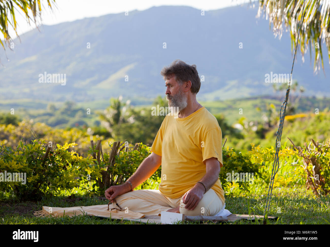 Ein Mann mit Bart auf Yoga Matte und Üben von Meditation mit mala Perlen in der Natur. Die Teilnahme an Exerzitien in Fidschi. Stockfoto