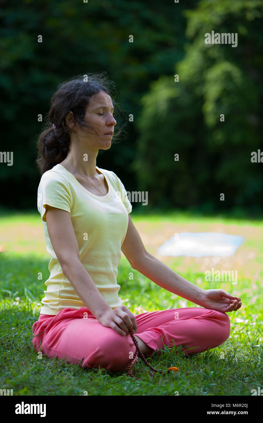 Eine junge Frau sitzt auf Gras im Park und die Praxis der Meditation mit mala Perlen. Stockfoto