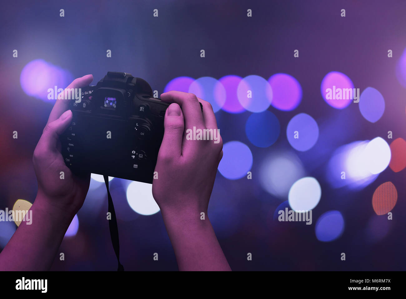 Kamera in der Hand und die Lichter der Stadt im Hintergrund. Lila Szene. Stockfoto