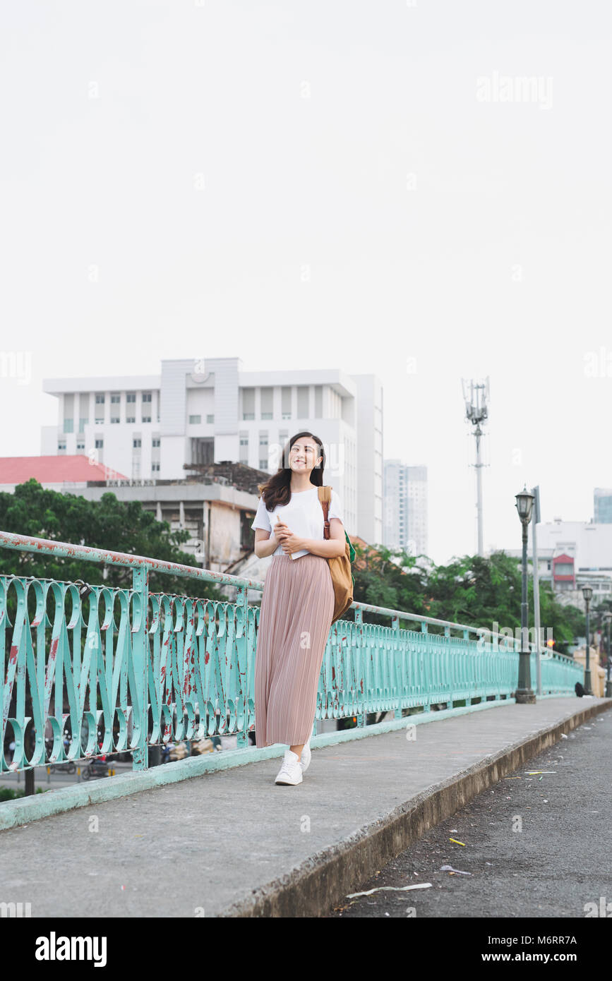 Volle Länge des asiatischen Mädchen gehen auf eine Brücke mit Blick auf die Stadt mit einem Buch in der Hand. Stockfoto