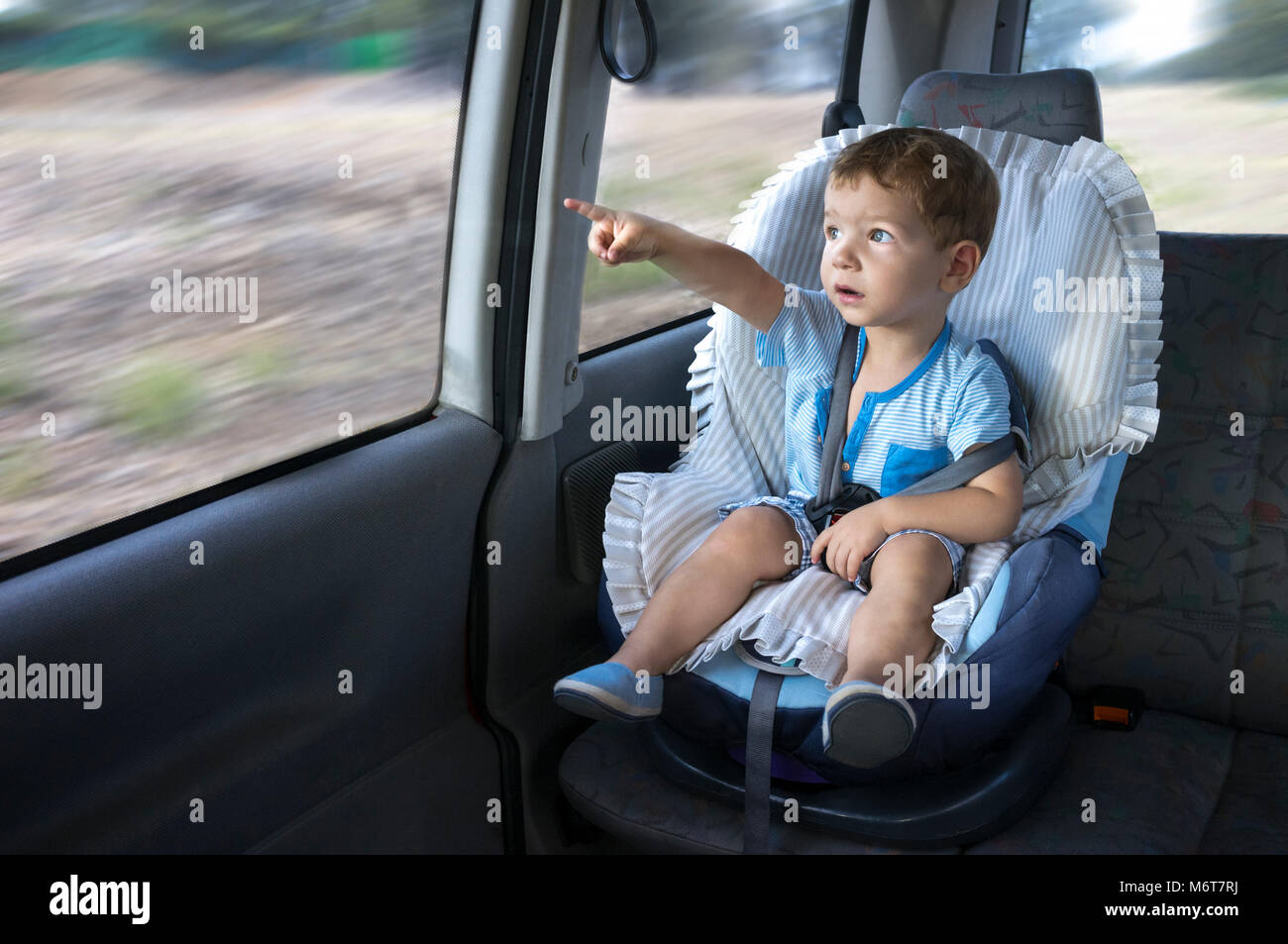 Cute little boy beobachten die Landschaft von seinem Auto Kindersitz. Er zeigt etwas Stockfoto