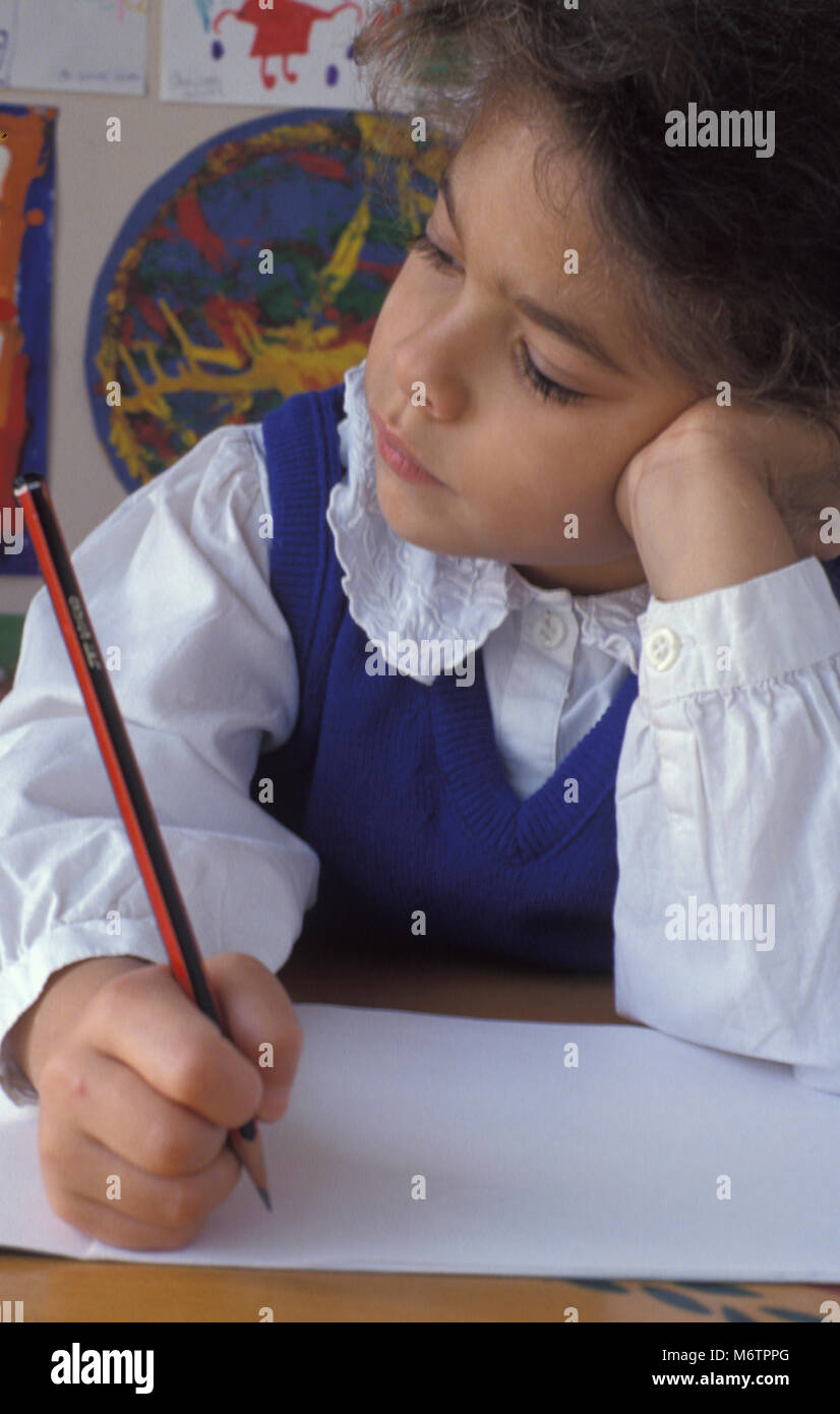 Kleines Mädchen am Schreibtisch über Bleistift und Papier nachdenken Sitzen Stockfoto