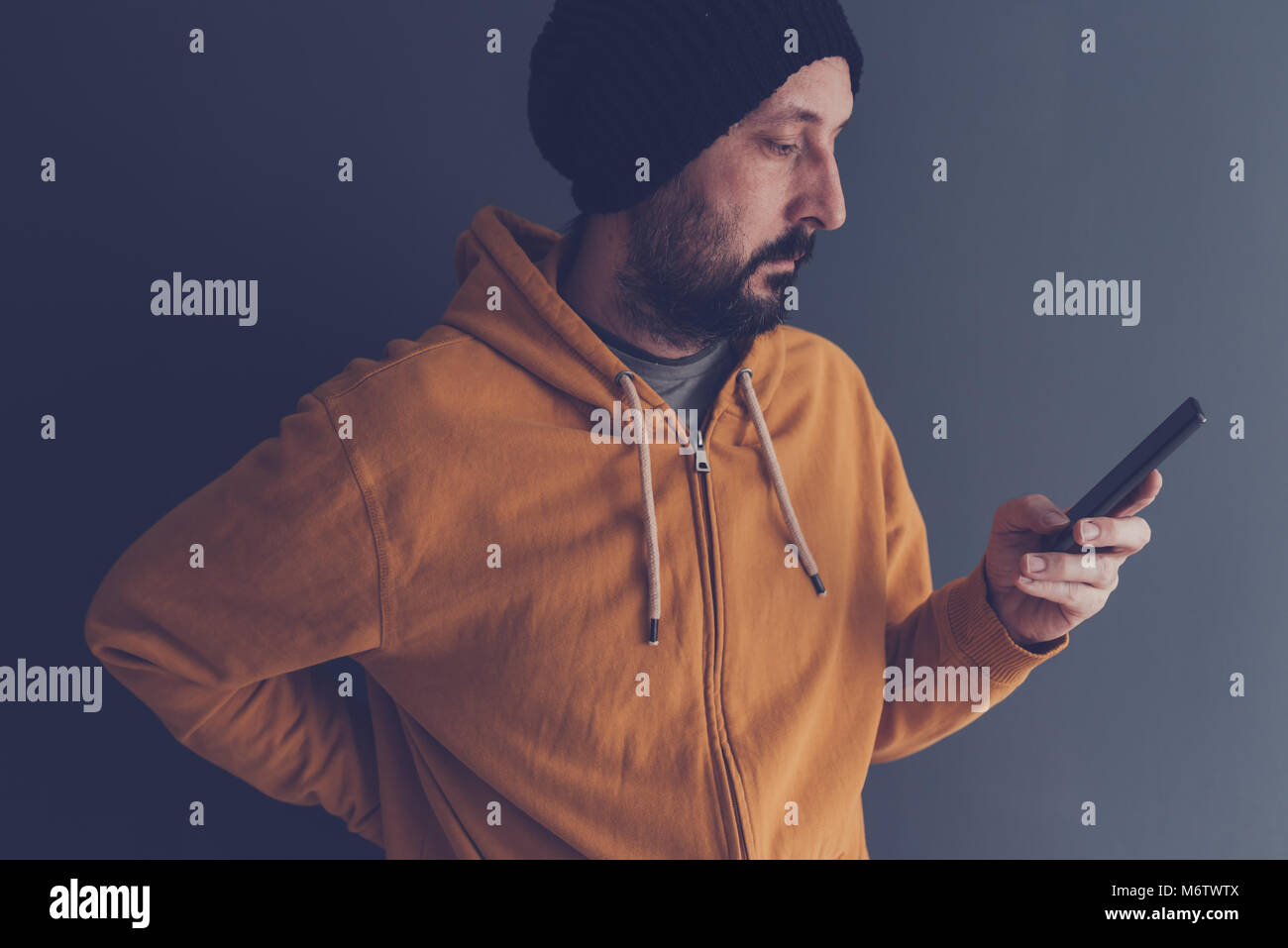 Casual erwachsenen Mann mit Kappe und gelben T-Shirt am Handy suchen, Low Key Kommunikation und Lifestyle Portrait mit selektiven Fokus Stockfoto