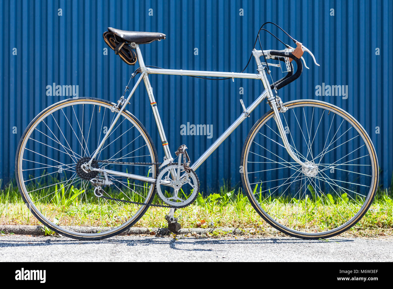 Vintage Racing Fahrrad aus den 60s mit Verchromter Stahlrahmen vor der blauen Wand und grünes Gras Stockfoto