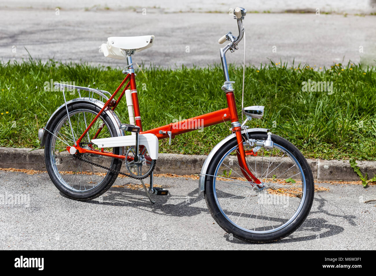 Vintage Classic 1970 s rotes Klapprad Fahrrad in einem einwandfreien Zustand Parken auf der Straße in der Nähe von Gras Stockfoto