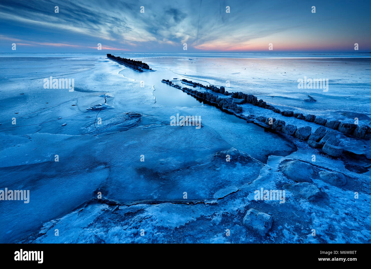 Alte hölzerne Wellenbrecher auf gefrorenen Küste in der Dämmerung Stockfoto