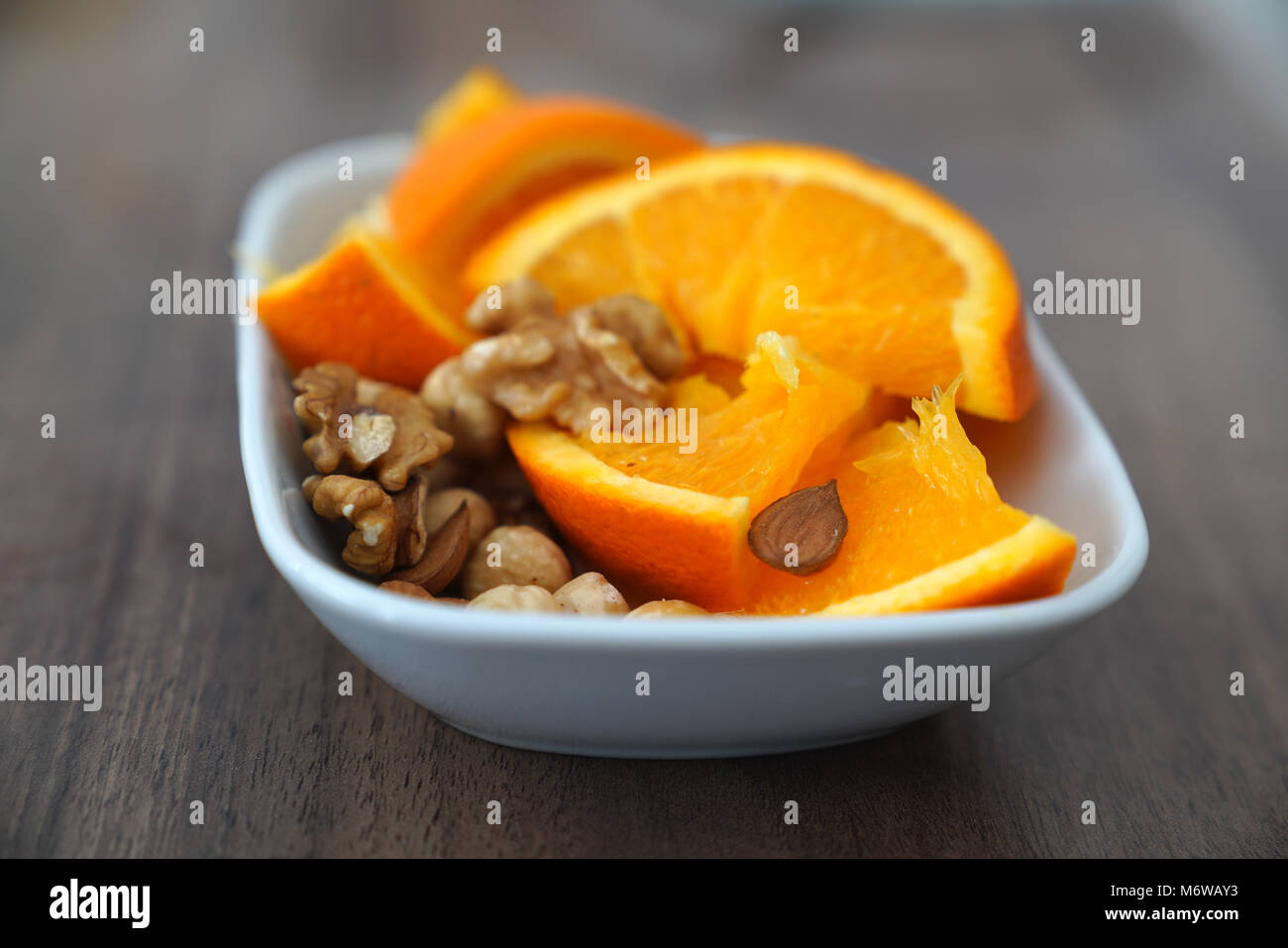 Orange in Scheiben und Muttern zusammen in eine Schüssel geben. Stockfoto