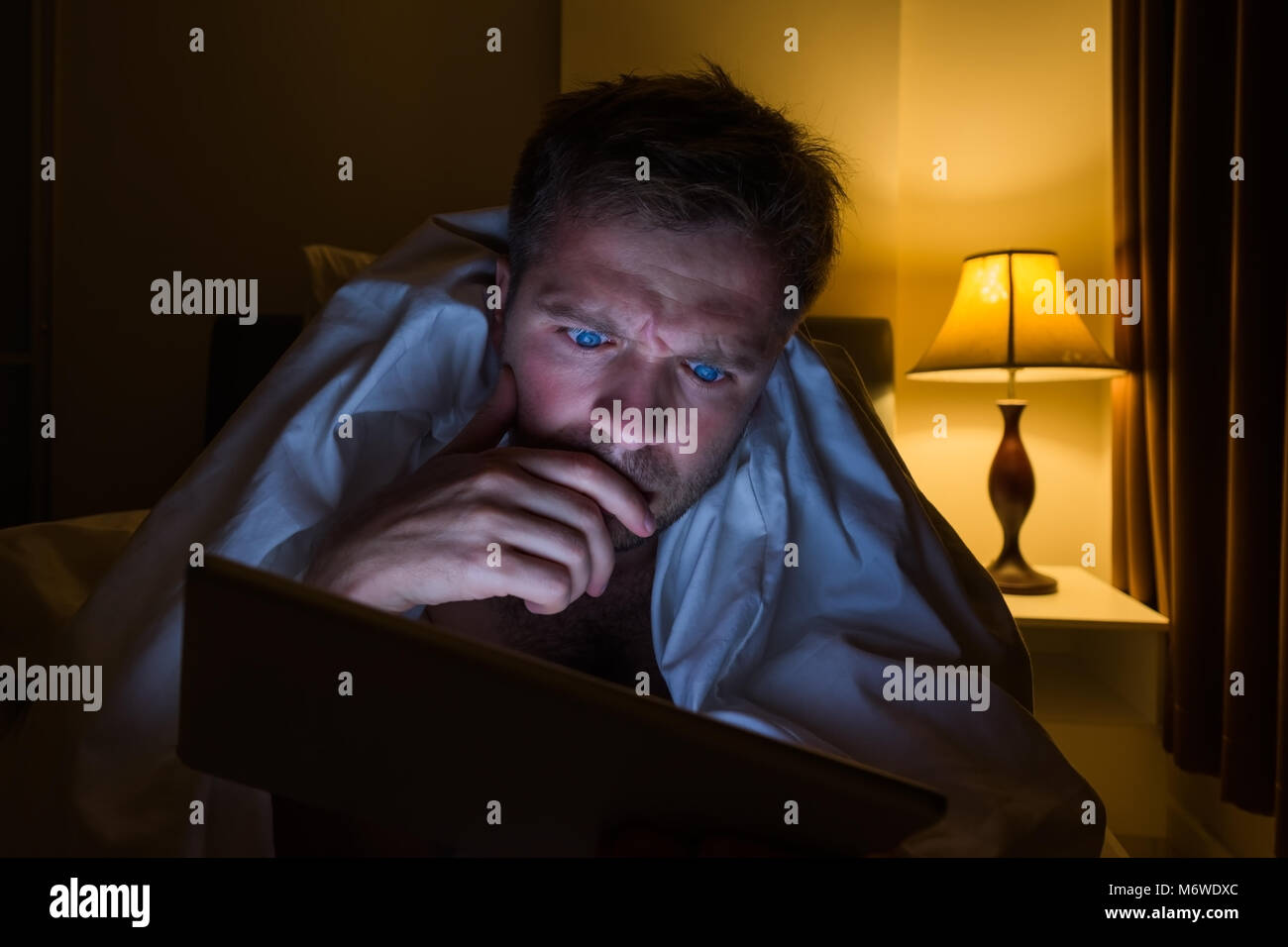 Hübscher junger Mann zu Hause lesen mit Tablet PC liegend auf Bett in der Nacht. Er ist müde und will schlafen Stockfoto