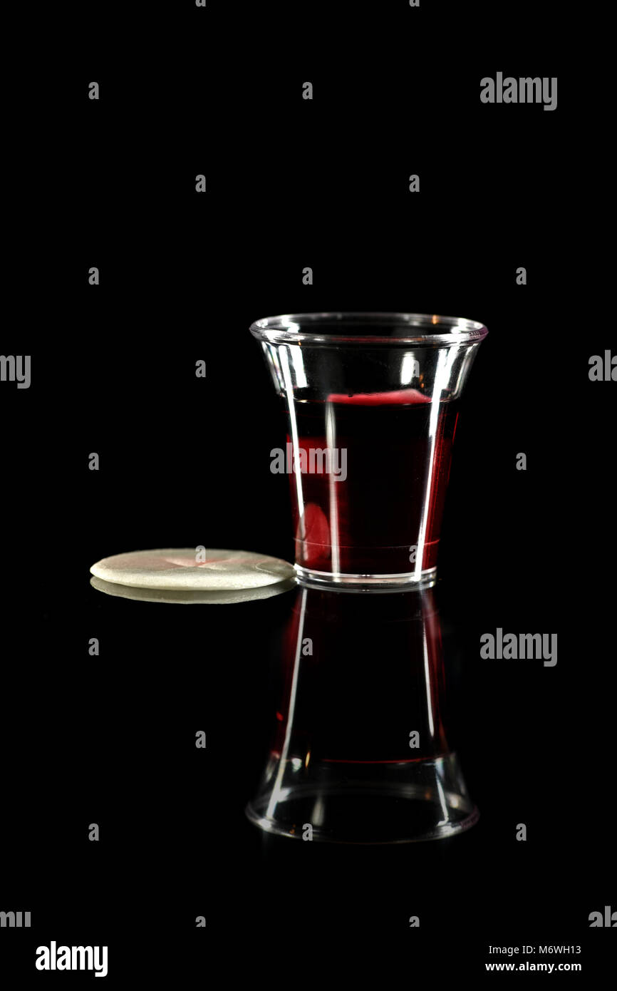 Abendmahlskelch mit Wein und Wafer auf reflektierenden Tisch auf dunklem Hintergrund Stockfoto