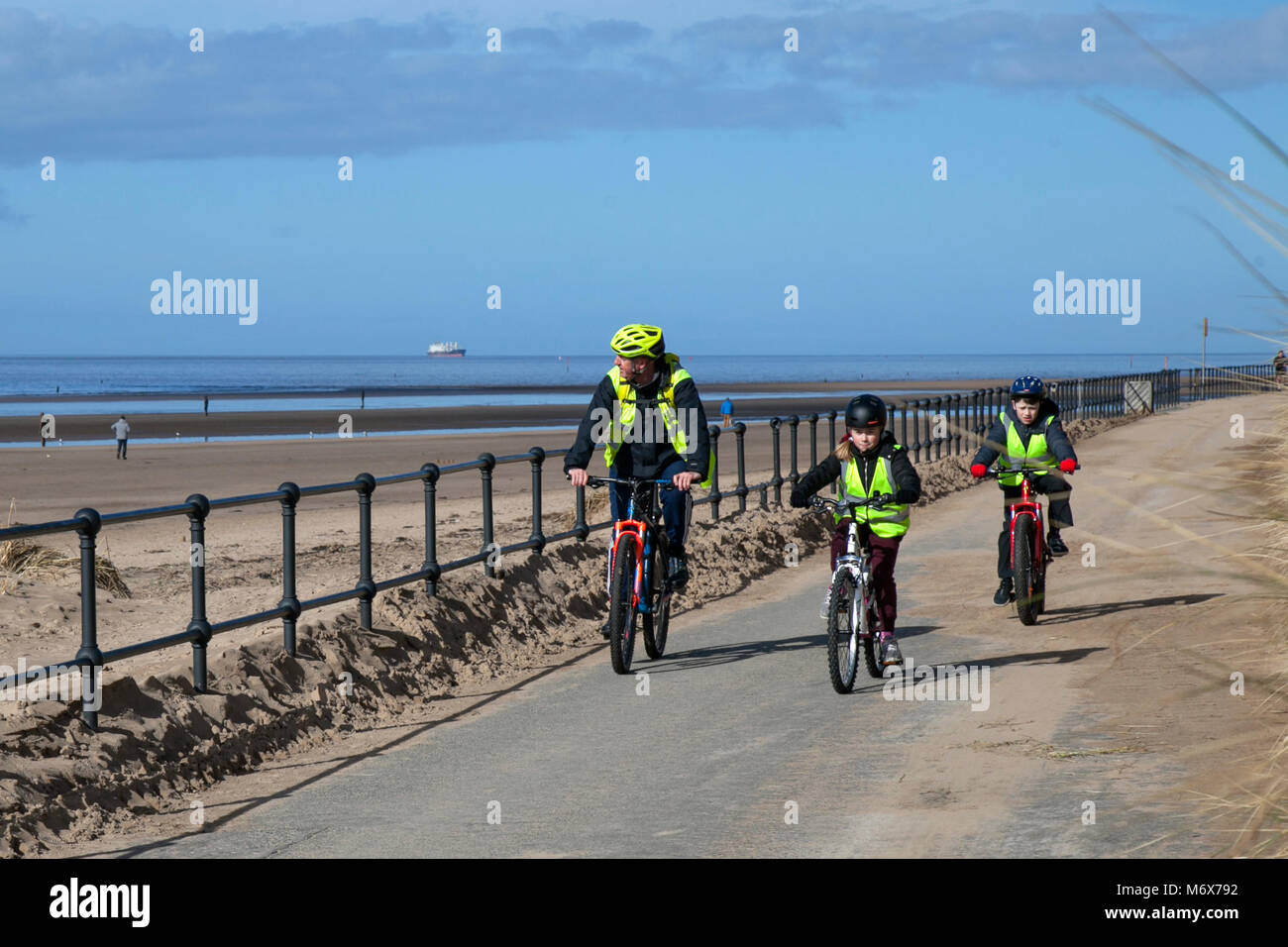 Kinder unter Anleitung Radfahren in Crosby, Merseyside. Wetter in Großbritannien. März 2018. Sonniger Start in den Tag auf dem Mariners Way, während Schulkinder auf dem Fahrrad auf dem Mariners Way an der Strandpromenade trainieren. Stockfoto