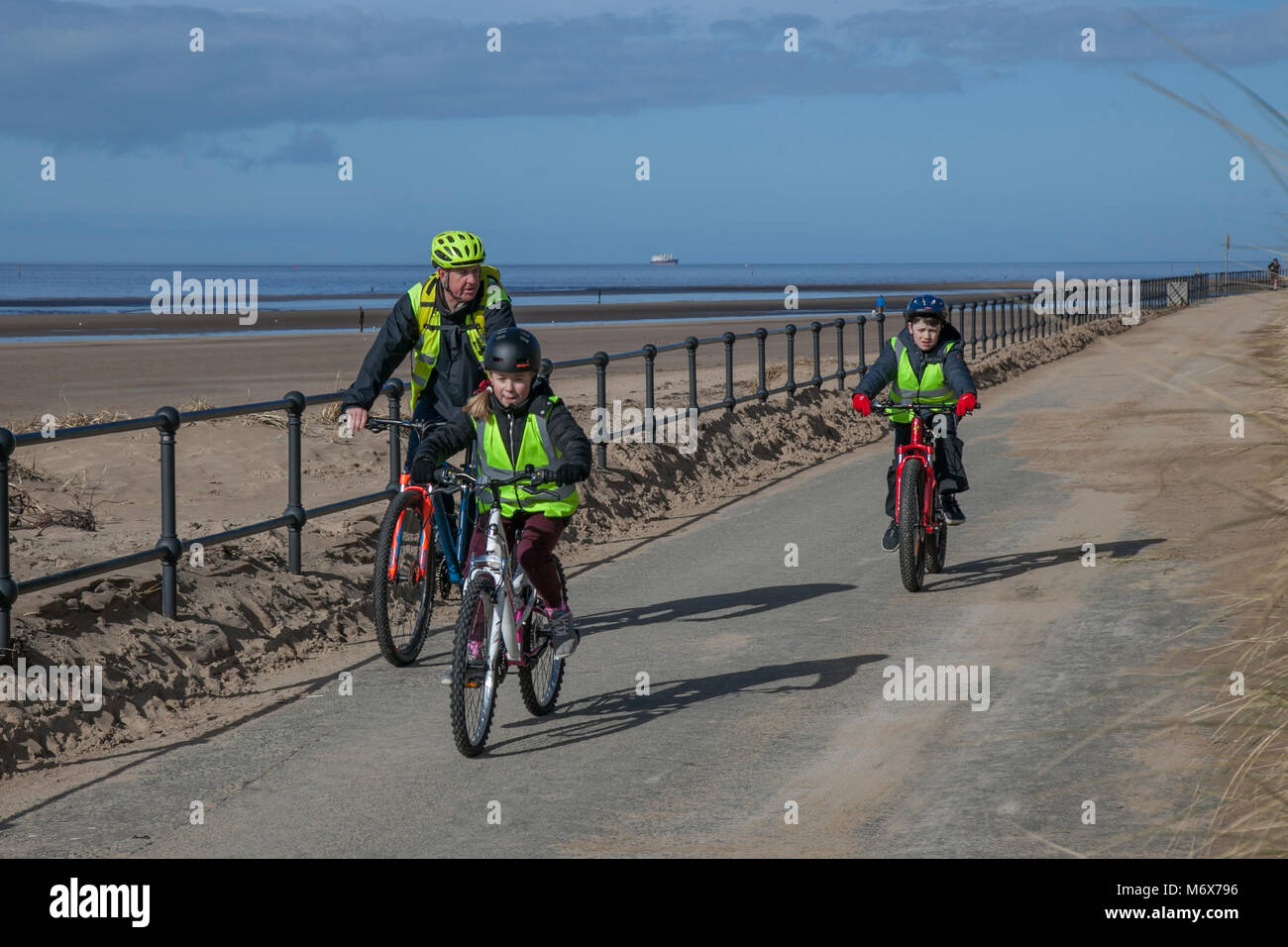 Kinder unter Anleitung Radfahren in Crosby, Merseyside. Wetter in Großbritannien. 7th. März 2018. Sonniger Start in den Ausflugstag auf dem Mariners Way, da Schulkinder auf dem Fahrrad auf dem Mariners Way am Meer trainiert werden. Stockfoto