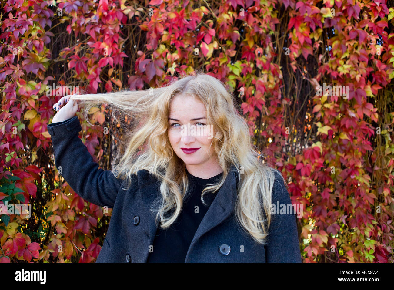 Die blonde Frau spielt mit ihren Haaren und stehen in bunten Park Stockfoto