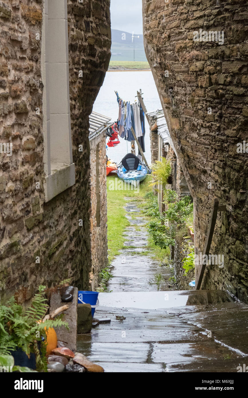 Sehr engen Durchgang zwischen Häusern in Stromness, Orkney, Schottland, UK, Gärten und das Wasser vorne Stockfoto