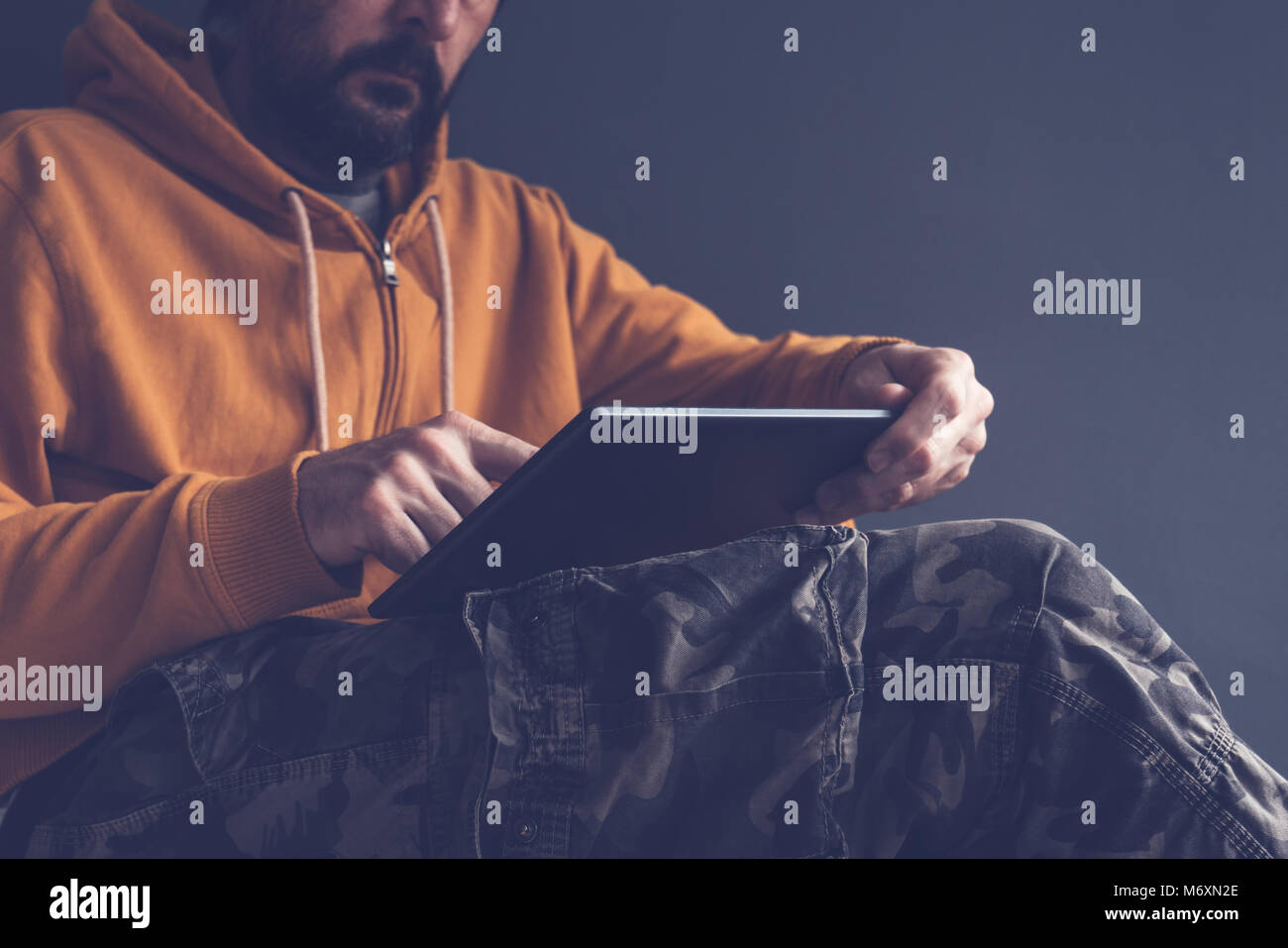 Legerer Mann mit digitalen Tablet laid back im Bürostuhl. Männliche Person tragen gelbe Hoodie und militärischen Hose ist mit modernen Computer Gerät. Stockfoto
