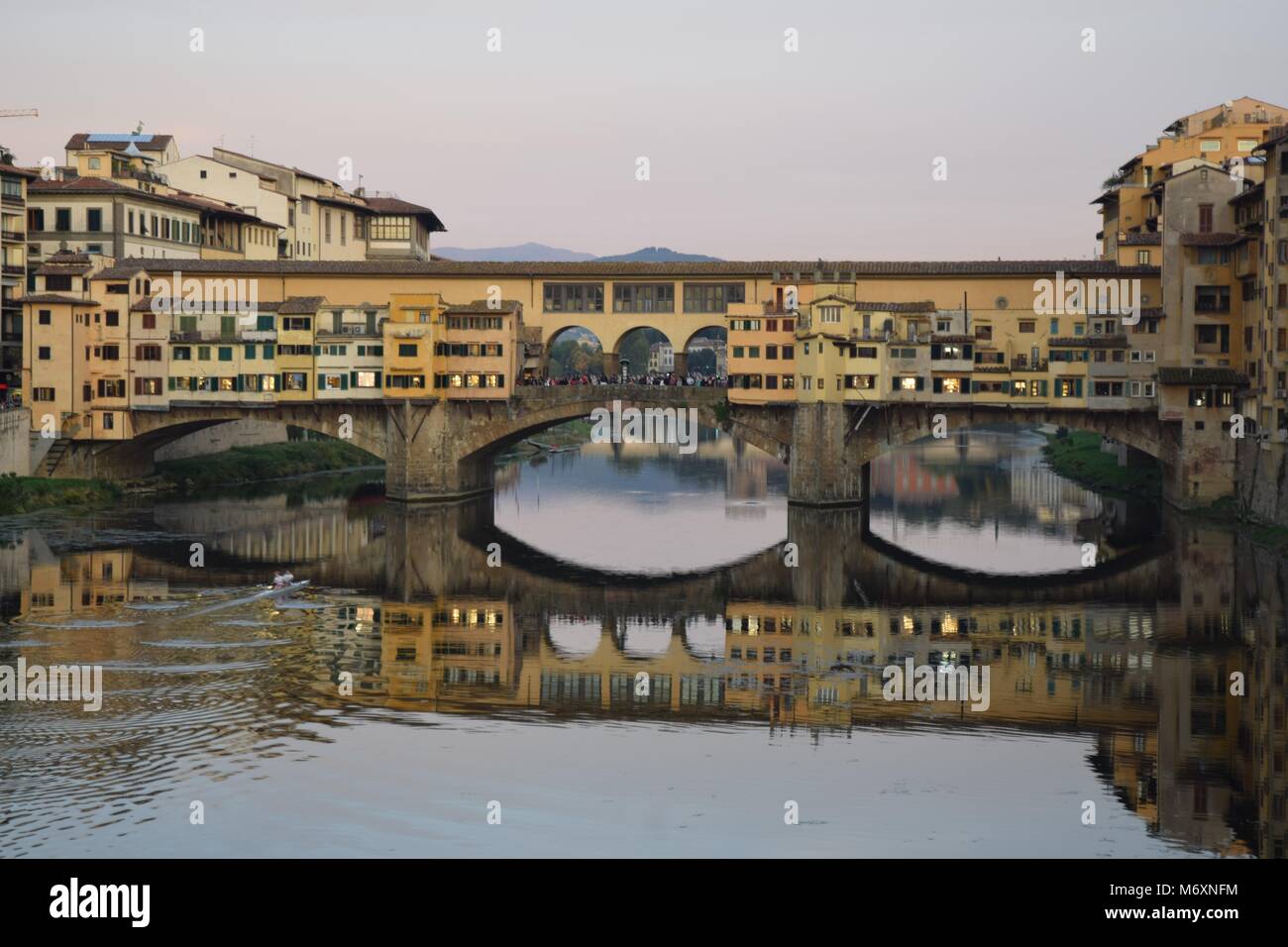 Brücke über den Arno: Ein Blick auf die Ponte Vecchio in Florenz, Toskana, während unten die Reflexion in der Arno ist durch zwei Ruderer durchbohrt. Stockfoto