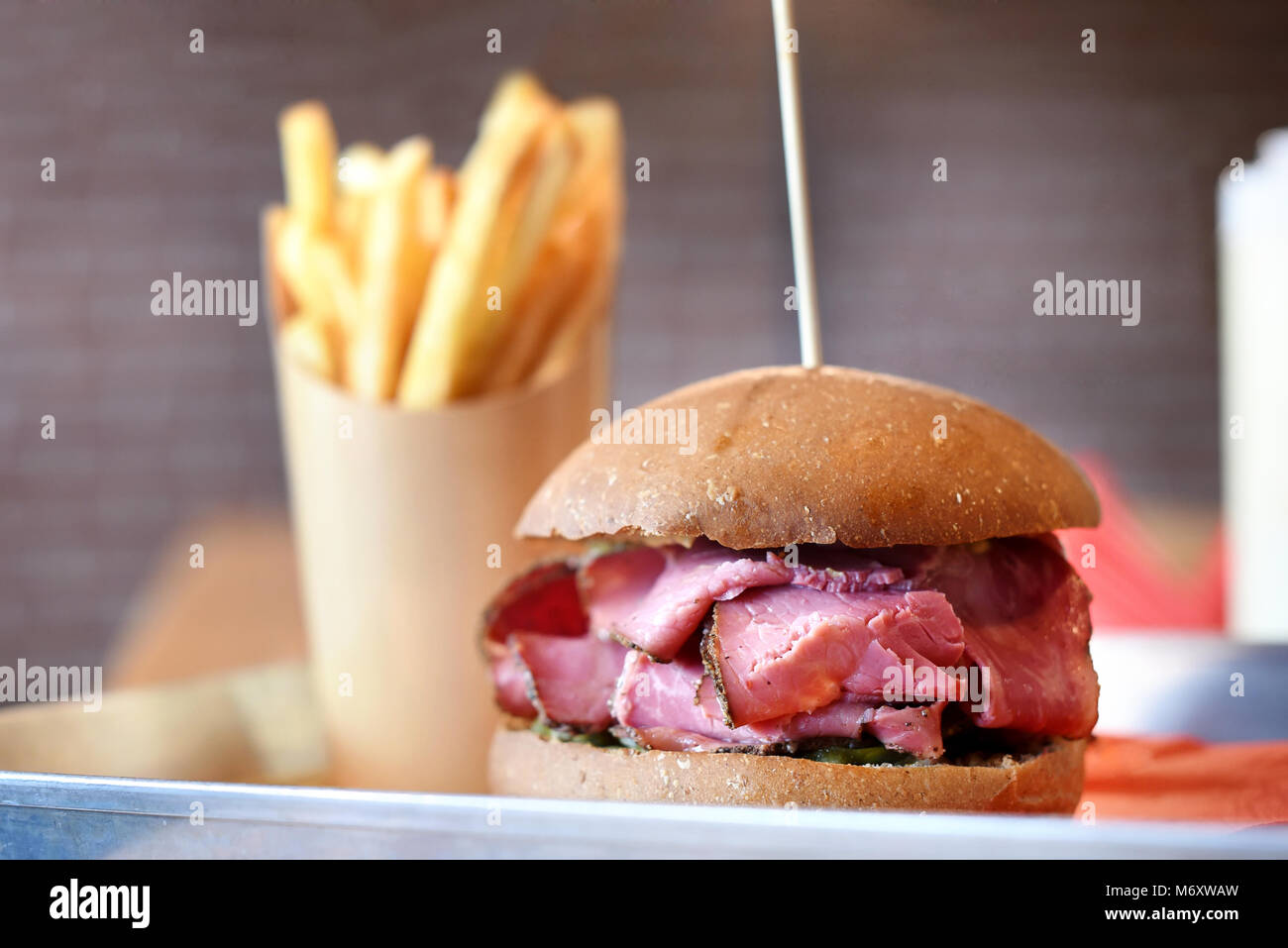 Pastrami Sandwich mit Schichten von geschnitten, gewürzt geräuchertem Rindfleisch auf ein knuspriges Brötchen mit Pommes frites serviert. Stockfoto