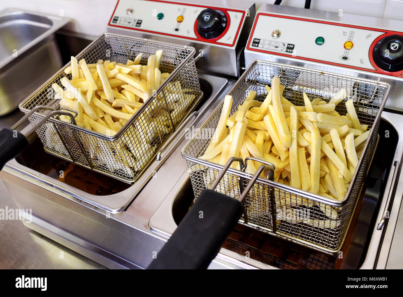 Knusprige Goldene Kartoffel Chips entleeren im Kabel metall Körbe auf eine elektrische Friteuse in der Küche eines Restaurants Stockfoto