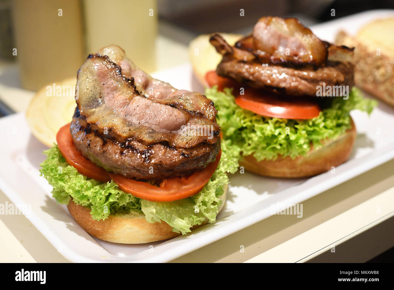 Vorbereitung eines Hamburger in einem Restaurant mit frischen Salat Garnituren, Rindfleisch Patty und Speck Speckscheiben auf einem weißen Brötchen auf ein fach geschichtet Stockfoto