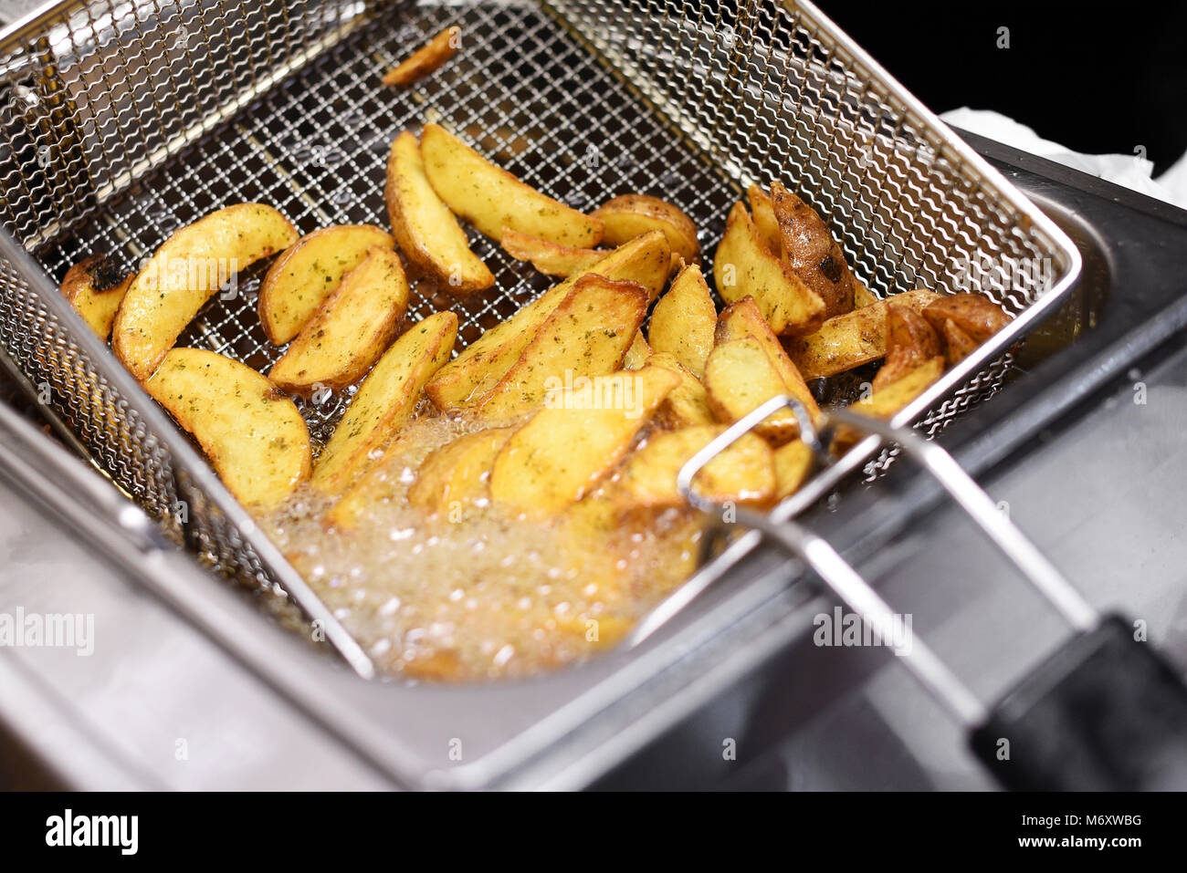 Würzige Kartoffelchips oder Keile kochen in einer Friteuse in Nahaufnahme der heißen sprudelnden Öl und Kabel metall Korb Stockfoto