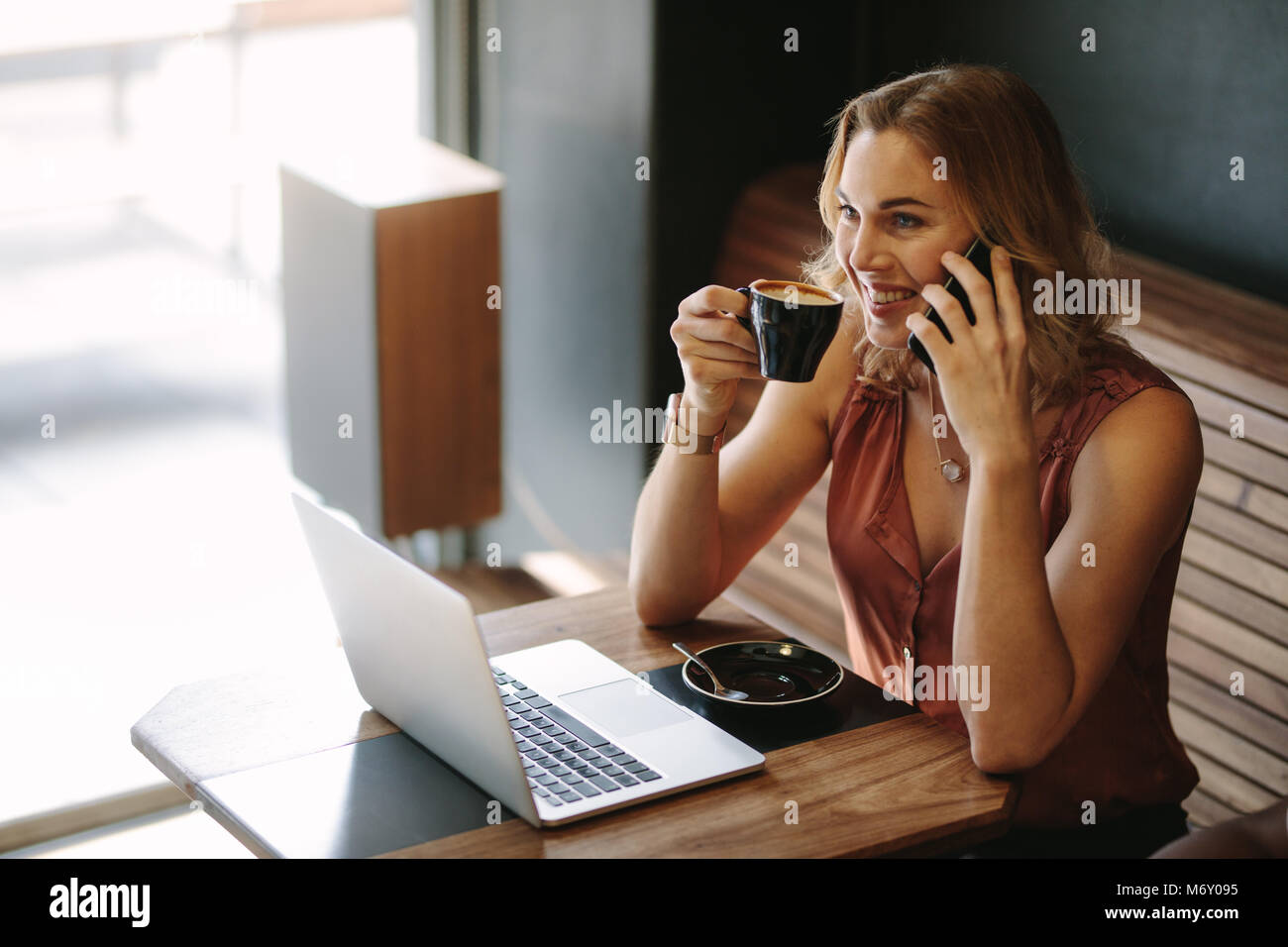 Freelancer sitzen in einem Café mit einem Laptop auf dem Tisch, während im Gespräch über Handy. Frau tun ihre Arbeit sitzend im Coffeeshop während Dr Stockfoto