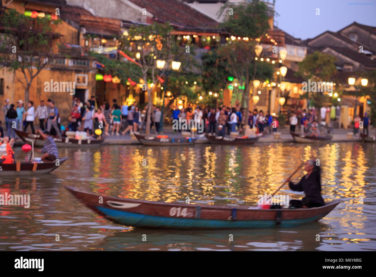 Eine ältere lokaler Mann Paddel sein Boot auf dem Thu Bon Fluss, mit Bach Dang Street im Hintergrund Stockfoto