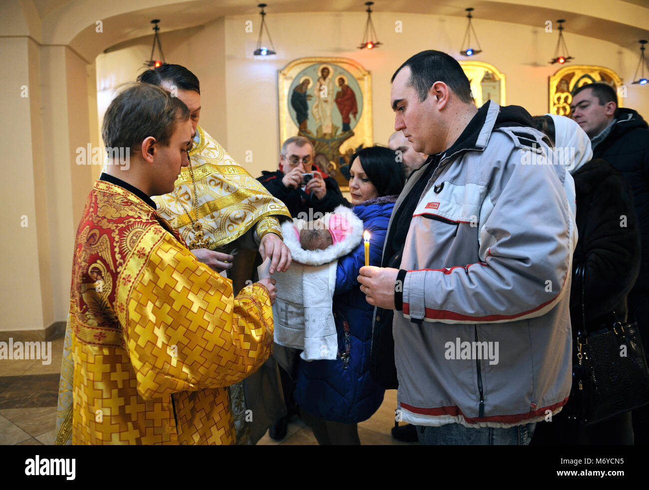 Taufe für Baby. Mann und Frau stehen mit einem Baby auf den Händen und der Priester schneidet einen Haarstreifen vom Kopf des Kindes ab. Januar 7,2018. Ukraine Stockfoto