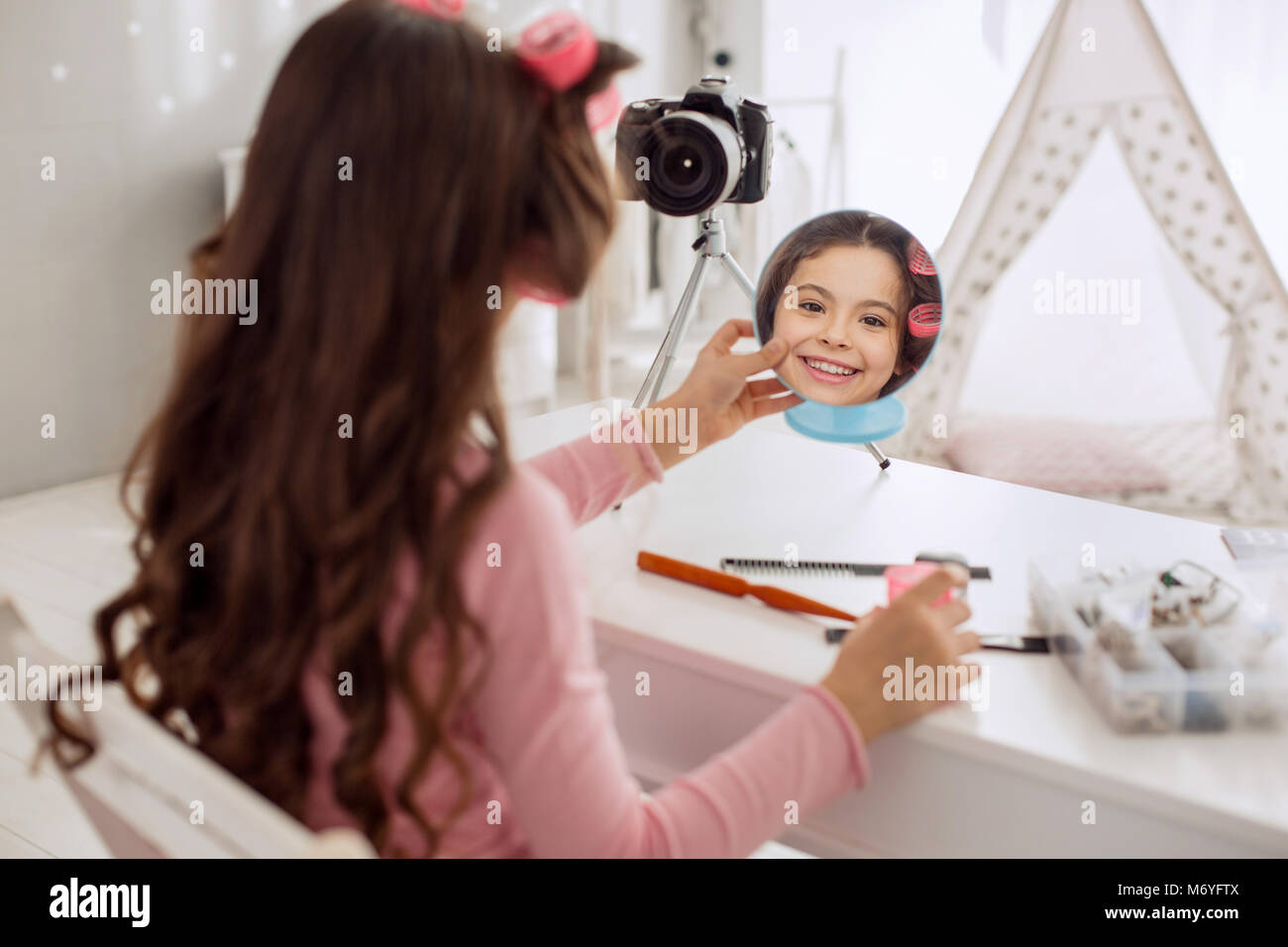 Fröhliches Mädchen schauen in Spiegel in Haar Walzen auf Stockfoto