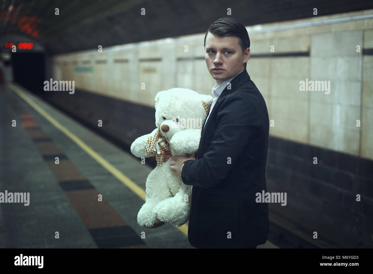 Traurige junge Mann mit einem Teddybär in seinen Händen steht in einer U-Bahn-Station. Stockfoto