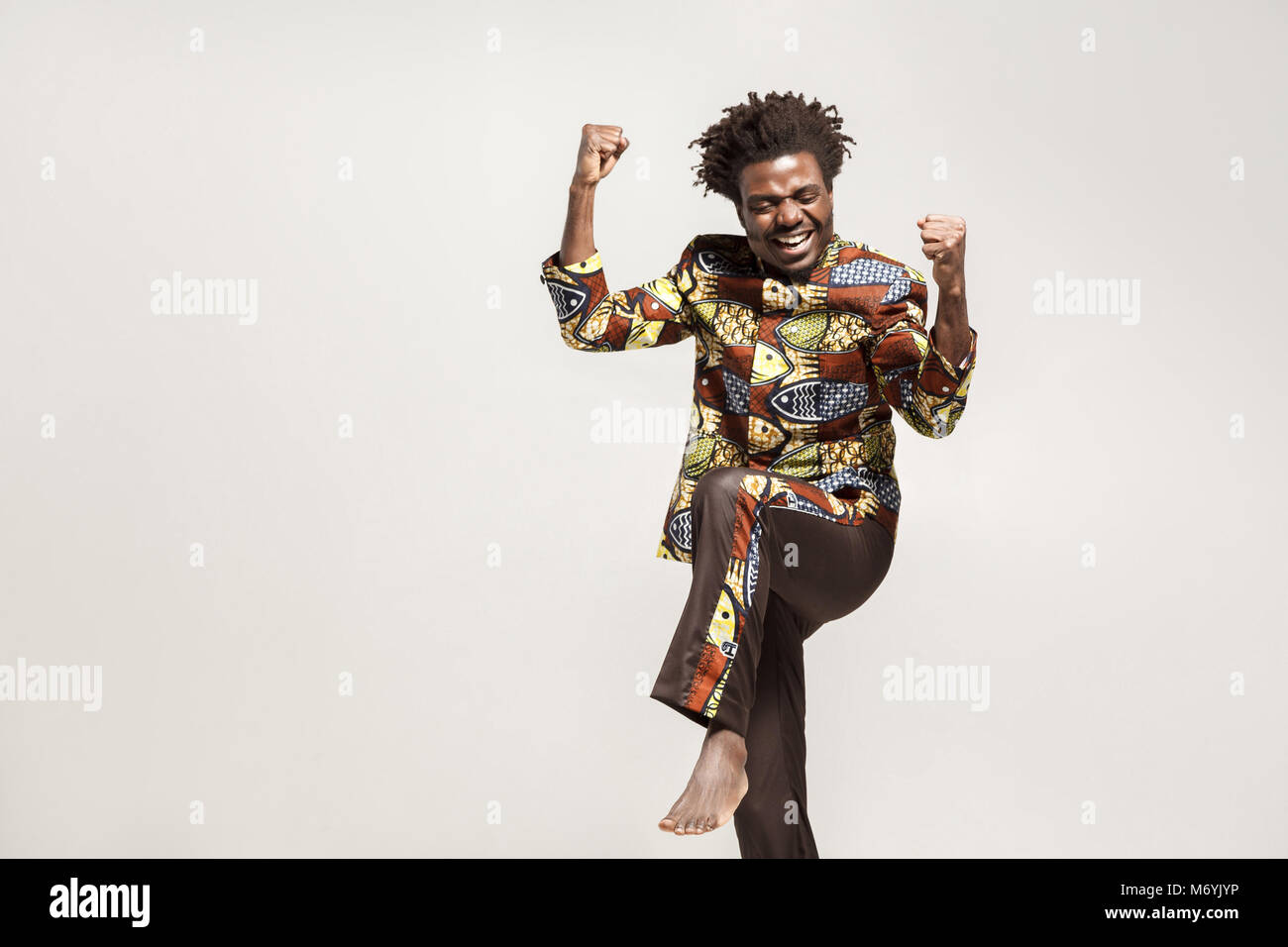 Ja! Ausdruck Glück afrikanischer Mann in traditioneller Kleidung Freude gewinnen. Innen, auf grauem Hintergrund Stockfoto