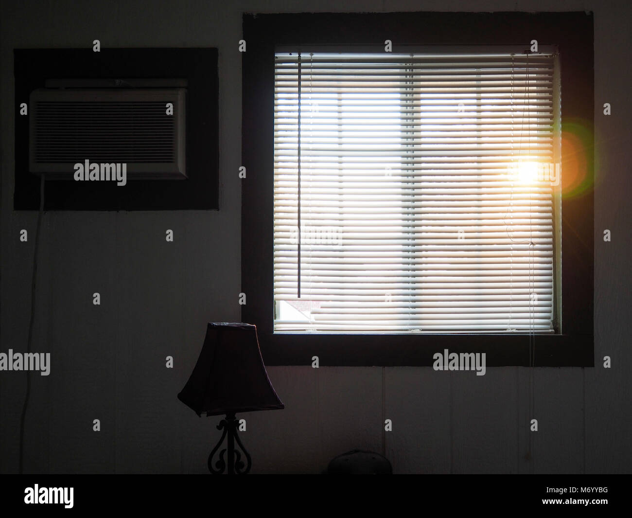 Die Sonne scheint durch die geschlossenen Persischen Jalousien eines Fensters in eine kaum eingerichtet gedimmt. Stockfoto