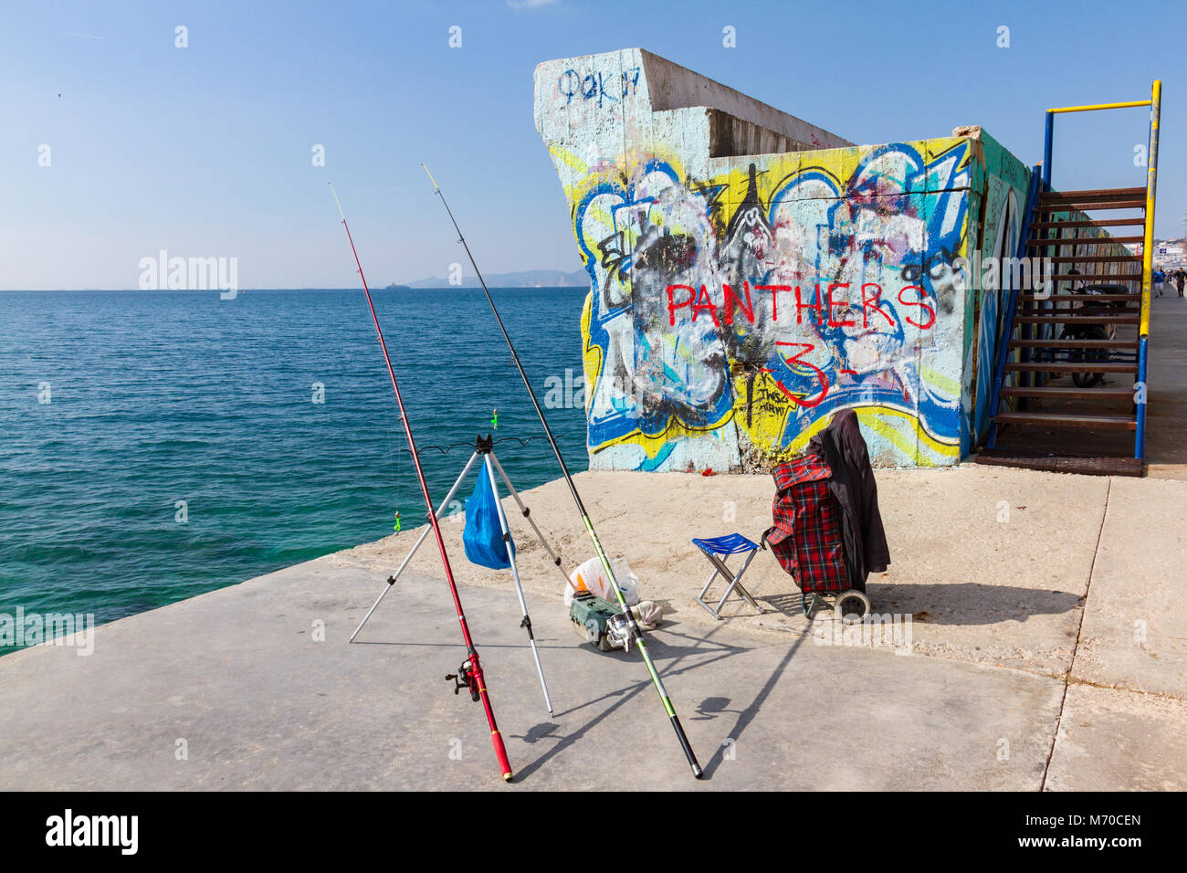 Athen, Griechenland - 17. Februar 2018: unbeaufsichtigt Angelruten an der Promenade gegen eine Wand mit Graffiti an Palaio Faliro in Athen, Griechenland Stockfoto