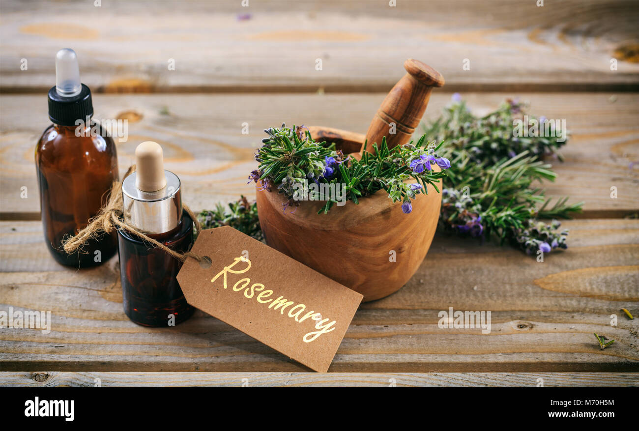 Rosemary wesentliches Öl und frischen blühenden Zweig in einem hölzernen Mörtel, Holztisch, Variable mit Text Rosmarin Stockfoto