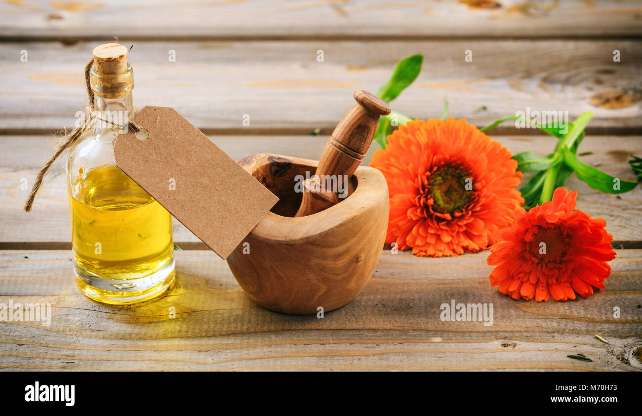 Ringelblume oder Pot marigold ätherisches Öl und frischen blühenden Zweig in einem hölzernen Mörtel, Holztisch, leeres Tag, Platz für Text Stockfoto