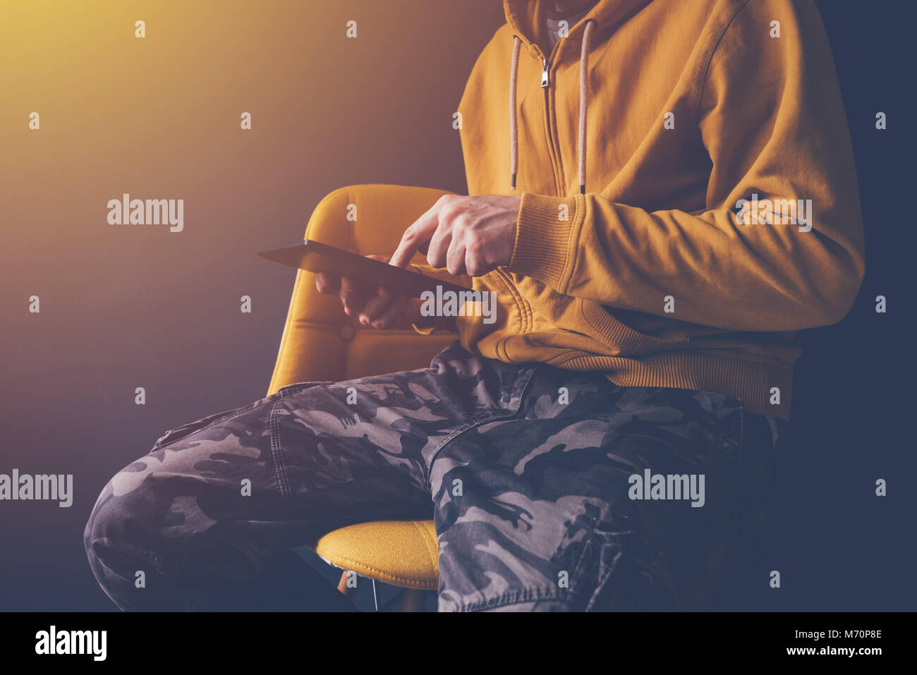 Legerer Mann mit digitalen Tablet laid back im Bürostuhl. Männliche Person tragen gelbe Hoodie und militärischen Hose ist mit modernen Computer Gerät. Stockfoto