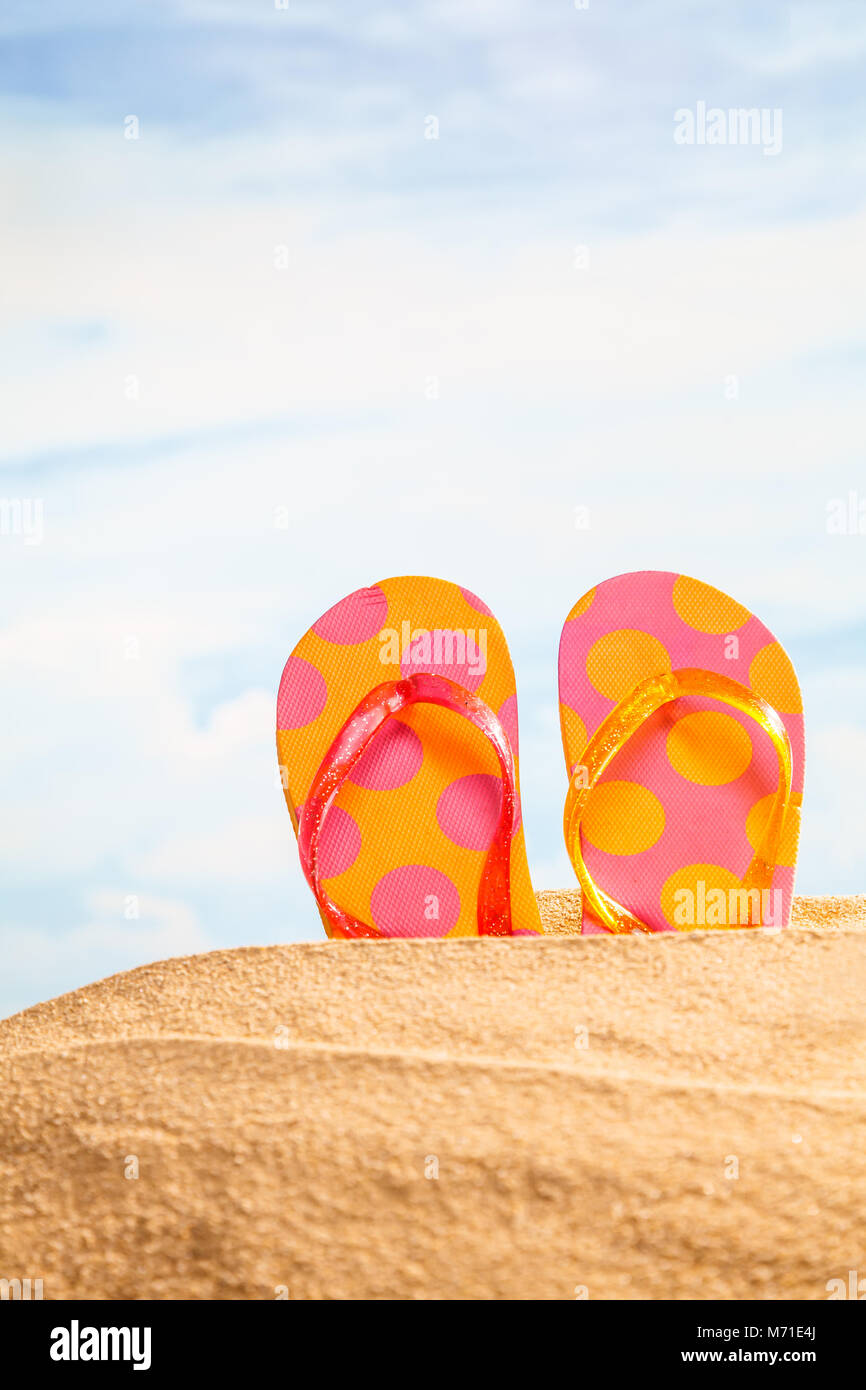 Sommer Saison, bunte spotty Sandalen oder Flip-flop am Sandstrand mit sonnigen bunten Hintergrund des blauen Himmels und Kopieren. Reisen und feeli Stockfoto