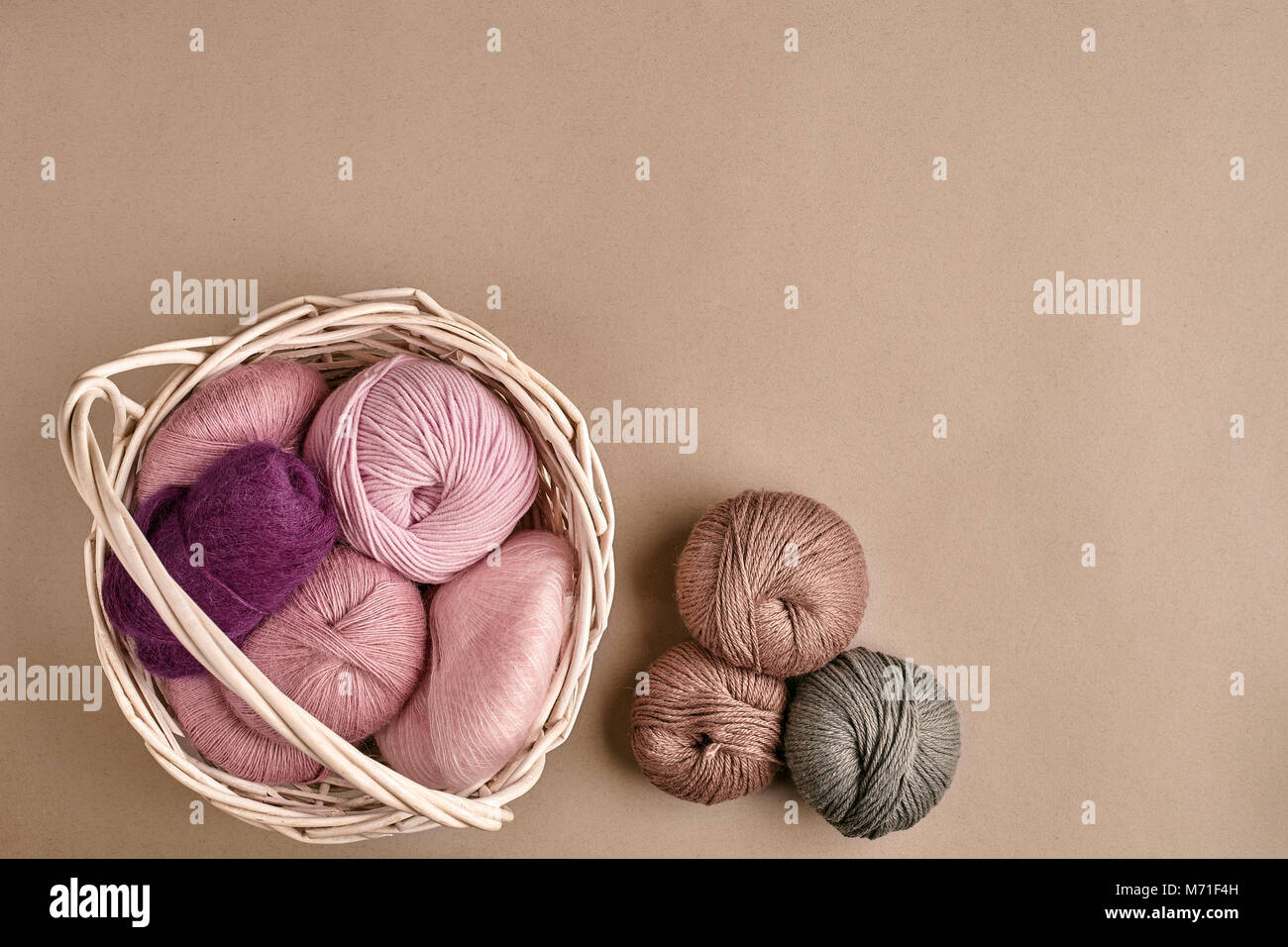 Kugeln von Garn und Stricknadeln. Farbige Garne zum Stricken in einem Korb Schale auf einem beigen Hintergrund. Stockfoto