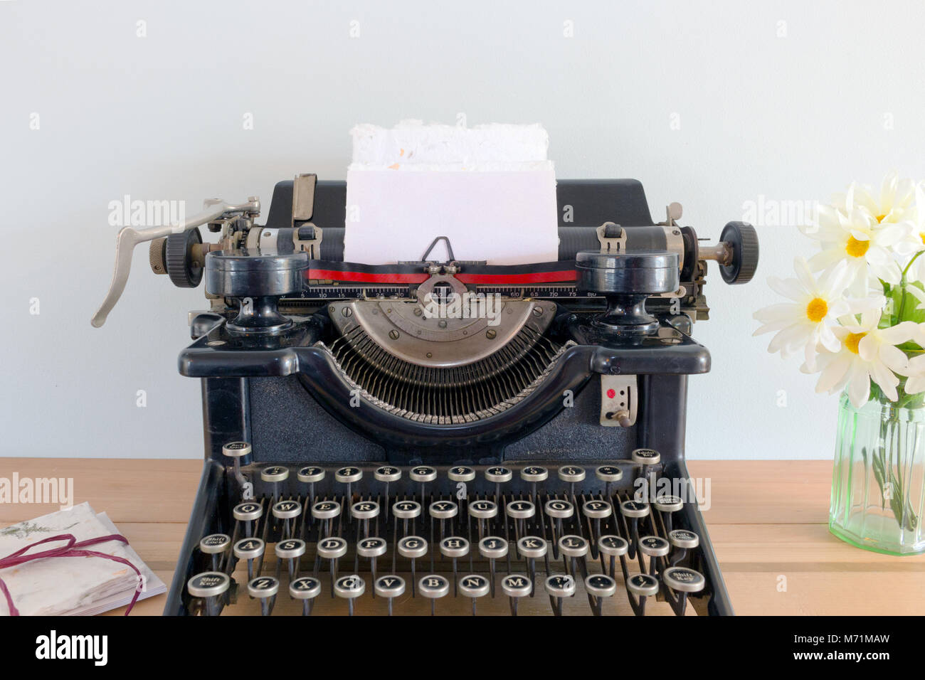 Antike Schreibmaschine mit leeren Papier in der Schlitten auf einem Holztisch mit Blumen und einem Bündel von beachten Sie Karten mit einem Bindfaden Stockfoto