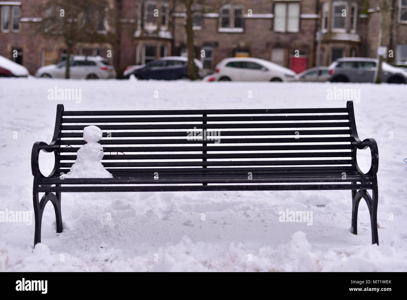 Einsame Schneemann auf einer Parkbank Stockfoto
