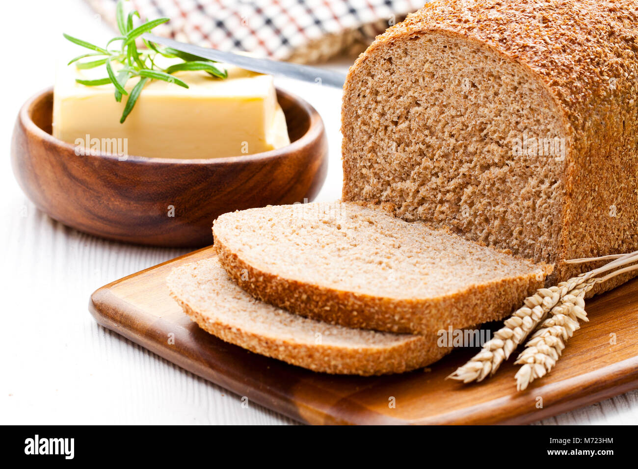 Langsam geschnitten - gebackene Bio Vollkorn Brot mit Butter und Rosmarin und Weizenähren Stockfoto
