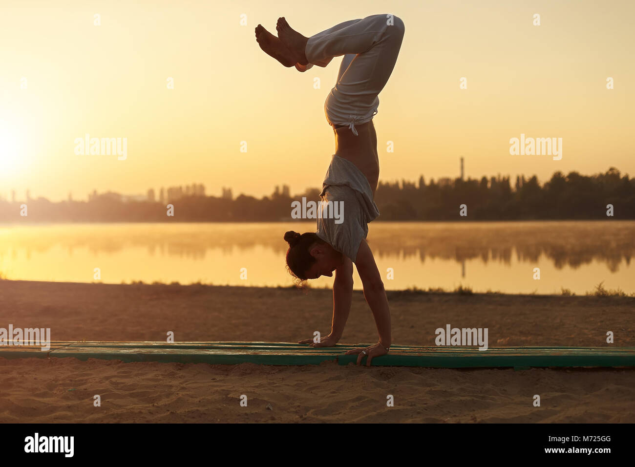 Konzept über Leute, Lifestyle und Sport. Capoeira am Strand, in der Nähe der See im Park ein Performer, bei Sonnenaufgang. Casual athletischen Mann in weißen Hosen Stockfoto