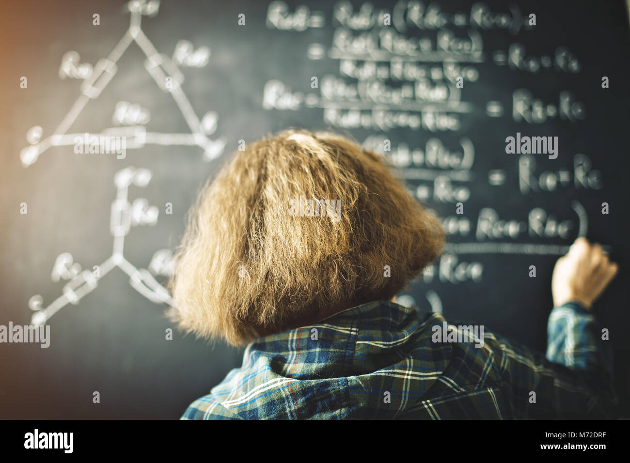 Der Lehrer schreibt an einer Tafel mit Kreide eine Formel für elektrischen Strom. Stockfoto