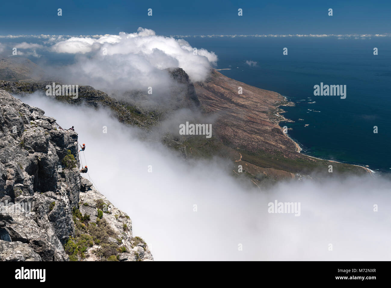 Abseilers Abseilen vom Gipfel des Tafelbergs mit Atlantikküste Kapstadts im Hintergrund. Stockfoto