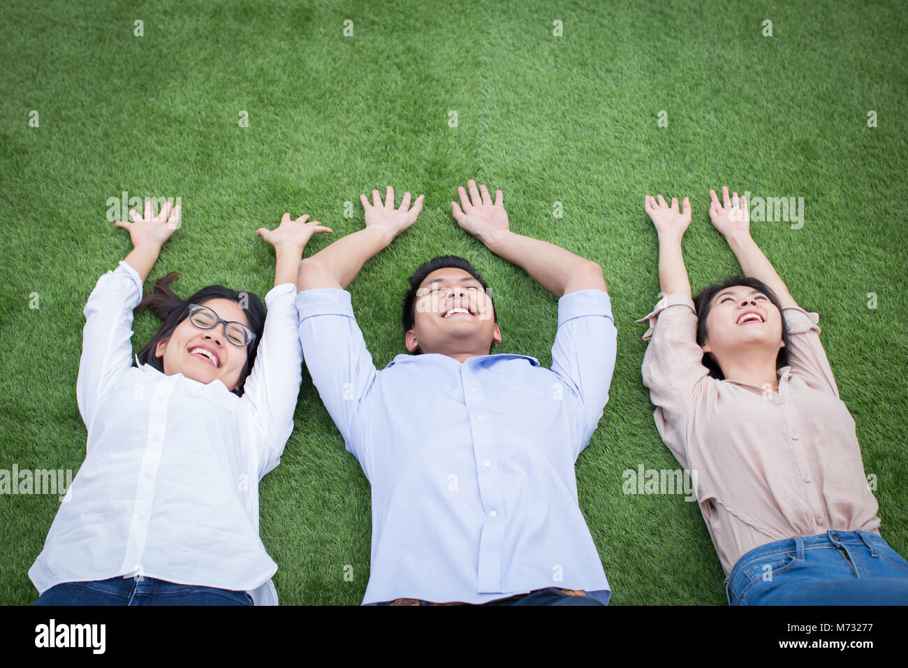 Gruppe von asiatischer Mann und Frauen feiern ihren Erfolg mit Händen und auf grünem Gras legen Stockfoto